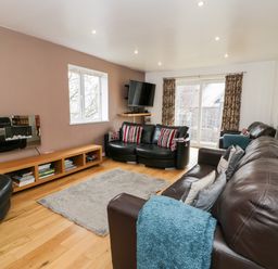 A living room with leather sofas a rug a wall-mounted TV and a wooden low shelf at Ty Coch in Llanberis