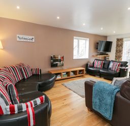 A living room with leather sofas and striped cushions a wooden floor and a wall mounted tv at Ty Coch in Llanberis