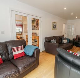 A living room with three brown leather sofas pillows and glass doors leading to another room at Ty Coch in Llanberis