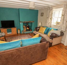 A living room with two sofas a wood burning stove curtains and a television at Snowdrop Cottage in Laugharne