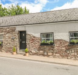 A single story stone cottage with three windows and a black door with potted plants outside at Snowdrop Cottage in Laugharne