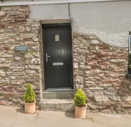 A stone cottage entrance with a black door two potted plants and a window with a planter box at Snowdrop Cottage in Laugharne