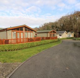 A paved road with small houses and green hedges along the side and trees in the background at The Retreat in Wisemans Bridge near Saundersfoot