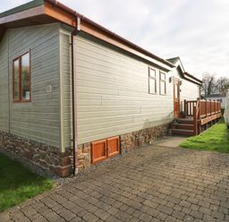 An exterior view of a single-story building with a wooden porch and paved pathway at The Retreat in Wisemans Bridge near Saundersfoot