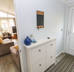 A hallway with a white cabinet next to a white door and a living room with sofas and a TV in the background at The Retreat in Wisemans Bridge near Saundersfoot