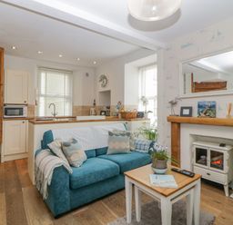 A living room with a blue sofa, a small wooden table, and a fireplace at Curlews Cottage in Looe