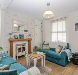 A living room with two blue sofas a small wooden coffee table a fireplace with a wooden mantel and a large mirror above it at Curlews Cottage in Looe