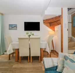 A dining area with a table and six chairs a wall-mounted TV and a corner with stairs at Curlews Cottage in Looe