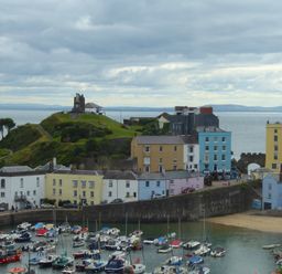 A harbor with boats docked near colorful buildings and a grassy hill with a monument and ocean view at 1 Beachtop Court Tenby
