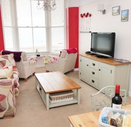 A living room with a patterned sofa two armchairs a wooden coffee table and a TV on a cabinet at 1 Beachtop Court in Tenby