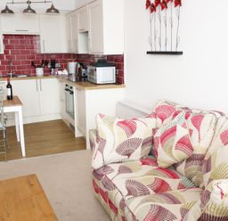 A kitchen and living area with white cabinets red tile backsplash patterned sofa wooden table and metal chairs at 1 Beachtop Court Tenby