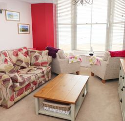A living room with patterned sofa two armchairs wooden coffee table and TV unit at 1 Beachtop Court in Tenby