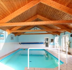 An indoor swimming pool with light blue walls wooden ceiling beams and tiled floor at Rookyard Cottage in Holton near Halesworth