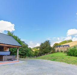 An outdoor area with a wooden shelter housing a hot tub a gate and trees near a grassy hillside at Ploony Hill Lodge in Bleddfa