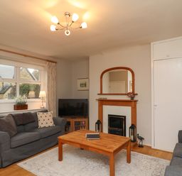 A living room with two sofas a wooden coffee table a fireplace a television and a window with curtains at Jasmine Cottage in Lesbury near Alnmouth