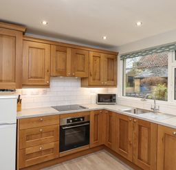 A kitchen with wooden cabinets a white refrigerator an oven a microwave a sink and a large window at Jasmine Cottage Lesbury near Alnmouth