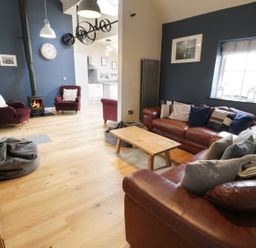 A living room with leather sofas cushions and a wooden coffee table next to a wood stove and burgundy armchairs at Horseshoe Cottage in Abersoch