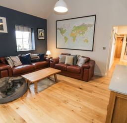 A living room with two brown leather sofas a wooden coffee table a gray bean bag a large world map on the wall and wooden flooring at Horseshoe Cottage in Abersoch