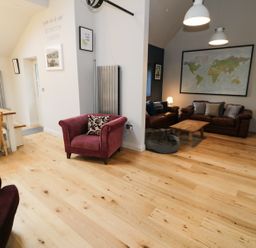An open living area with wooden floor a red armchair a dining table with wooden chairs leather sofas a wooden coffee table and a world map on the wall at Horseshoe Cottage in Abersoch