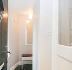 A small hallway with a dark door open a white wall a mirror a bench and a coat hook at Ramblers Roost in Grasmere