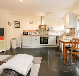 A kitchen and dining area with a wooden table and chairs a television on a colorful cabinet and kitchen appliances at Ramblers Roost in Grasmere
