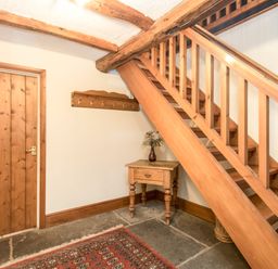 A wooden staircase next to a small wooden table with a vase and coat hooks mounted on the wall at Riven Oak in Lyth Valley near Levens