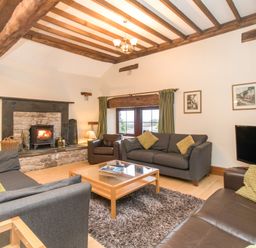 A living room with a stone fireplace wooden beams sofas coffee table and a television at Riven Oak in Lyth Valley near Levens