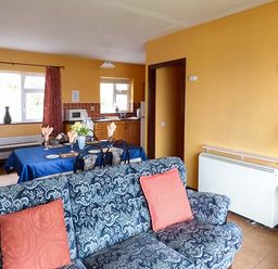 A living room with a patterned blue sofa and orange pillows and a dining table with a blue tablecloth at Rossbeigh Beach Cottage No 6 Rossbeigh near Glenbeigh County Kerry