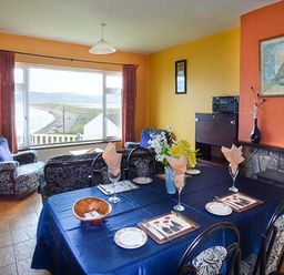 A dining room with a table set for four next to a seating area with armchairs and a window with a view at Rossbeigh Beach Cottage No 6 Rossbeigh near Glenbeigh County Kerry