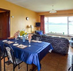 A dining area with a table set with plates and glasses next to a living room with sofas and a window view at Rossbeigh Beach Cottage No 6 Rossbeigh near Glenbeigh County Kerry