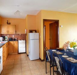 A kitchen and dining area with wooden cabinets white appliances and a dining table with blue tablecloth at Rossbeigh Beach Cottage No 6 Rossbeigh near Glenbeigh County Kerry