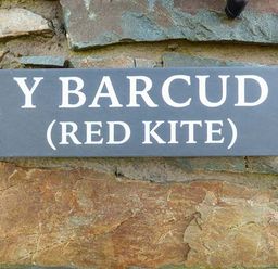A sign on a stone wall with the text Y Barcud Red Kite at Y Barcud in Holyhead