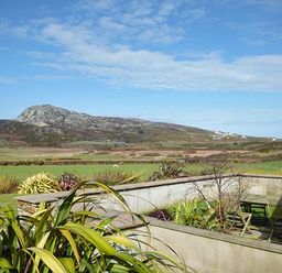 An outdoor patio area with table and chairs surrounded by plants with hills and fields in the background at Y Barcud in Holyhead