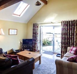 A living room with two sofas a wooden coffee table a floor lamp and a TV near glass doors at Y Barcud in Holyhead