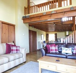 A living room with two sofas and a wooden coffee table under a wooden balcony at Y Barcud in Holyhead