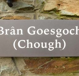 A brown rectangular sign with white text that reads Bran Goesgoch Chough mounted on a stone wall at Bran Goesgoch in Holyhead