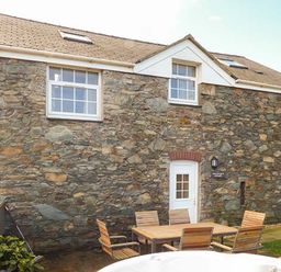 A stone exterior wall of a building with a white door and windows and wooden chairs around a wooden table at Bran Goesgoch in Holyhead