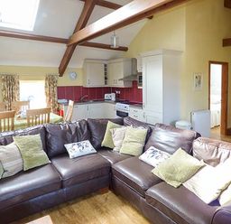 An open plan living area with brown leather sofas and a kitchen with white cabinets and red backsplash at Bran Goesgoch in Holyhead
