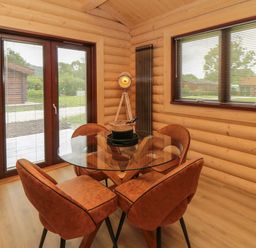 A dining area with a glass table and four brown chairs near windows and wooden walls at Carlton Lodge 1 in Stokesley
