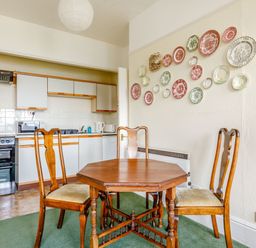A kitchen with white cabinets a black stove a wooden table with three chairs and decorative plates on the wall at Clooneavin Apartment 3 in Lynmouth near Lynton