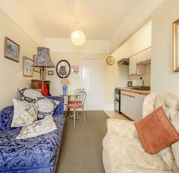A living area with a blue patterned sofa, cream armchair, table with two chairs, and a kitchenette at Clooneavin Apartment 5 in Lynmouth near Lynton