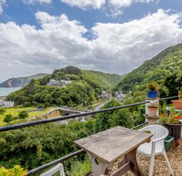 A terrace with plastic chairs and potted plants overlooking green hills and a coastal village at Clooneavin Apartment 8 Lynmouth near Lynton