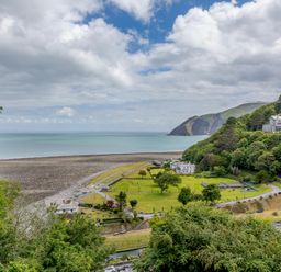 A coastal landscape with green fields trees a pebble beach and hills in the background at Clooneavin Apartment 8 Lynmouth near Lynton