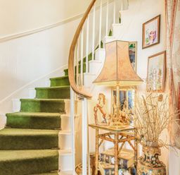 A curved staircase with green carpet and white railing next to a small table with a lamp horse figurine and decorative vase at Clooneavin Apartment 8 in Lynmouth near Lynton