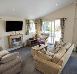 A living room with sofas a coffee table a wall-mounted television and sliding glass doors at Clearview Lodge in Borth