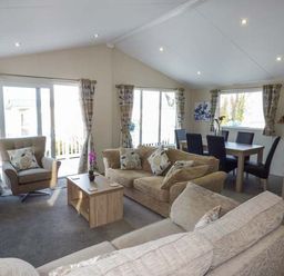 A living room with sofas armchair coffee table dining table with chairs and windows with curtains at Clearview Lodge in Borth