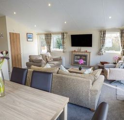 A living room with beige sofas a wall mounted television and flowers on a table at Clearview Lodge in Borth