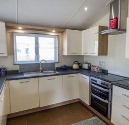 A kitchen with white cabinets black countertops a window stove kettle and toaster at Clearview Lodge in Borth