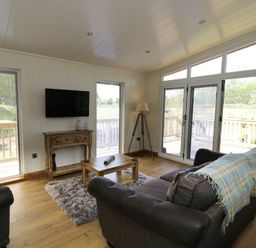 A sitting room with sofas a wooden coffee table a rug a wall mounted television and large windows at Squirrel Lodge in Gargrave near Skipton