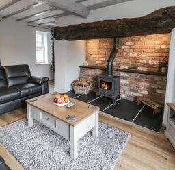 A living room with a wood stove fireplace leather sofas wooden coffee table and a television at Bryndan in Machynlleth